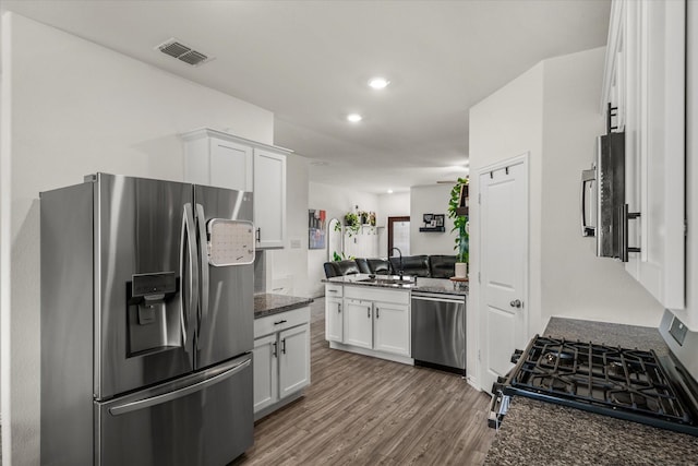 kitchen with wood-type flooring, sink, white cabinets, dark stone counters, and stainless steel appliances