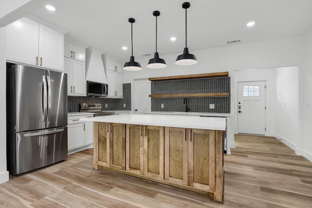 kitchen with white cabinetry, decorative light fixtures, stainless steel appliances, and a kitchen island