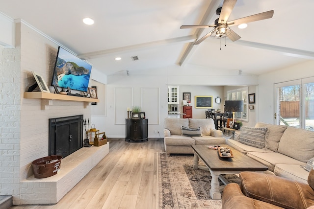 living room with ceiling fan, a brick fireplace, lofted ceiling with beams, and light hardwood / wood-style flooring