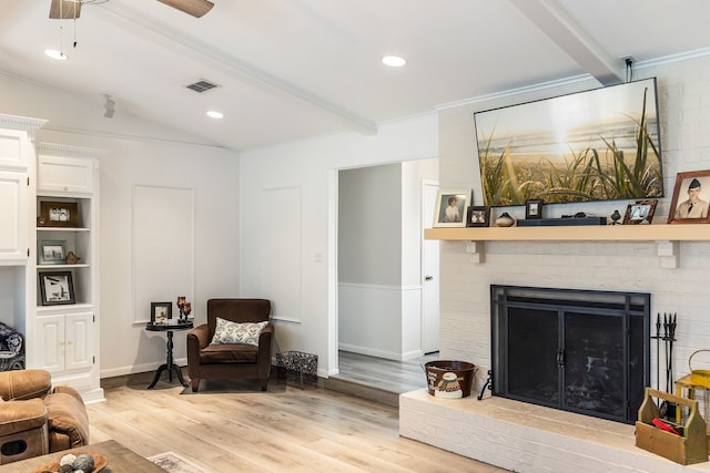 living room with crown molding, ceiling fan, a fireplace, lofted ceiling with beams, and light hardwood / wood-style floors