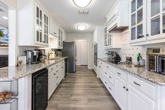 kitchen featuring light hardwood / wood-style flooring, white cabinetry, stainless steel appliances, wine cooler, and light stone countertops