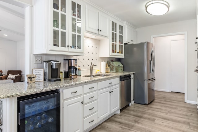 kitchen with sink, appliances with stainless steel finishes, wine cooler, white cabinets, and light wood-type flooring