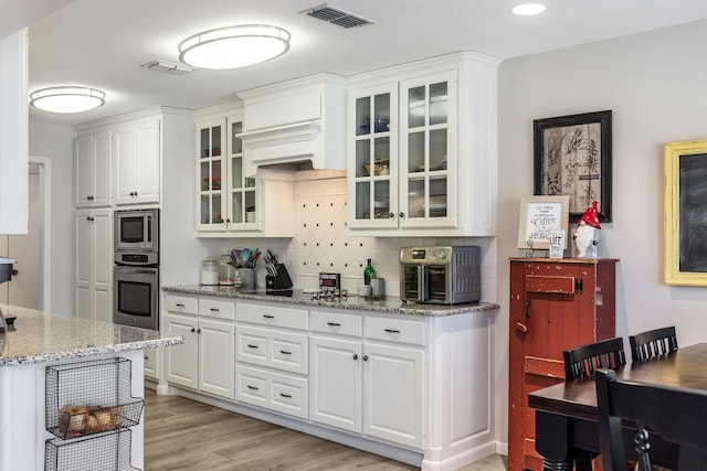 kitchen with white cabinetry, stainless steel appliances, light stone counters, tasteful backsplash, and light wood-type flooring