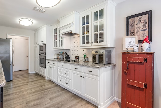 kitchen featuring appliances with stainless steel finishes, white cabinets, light stone counters, and light hardwood / wood-style flooring