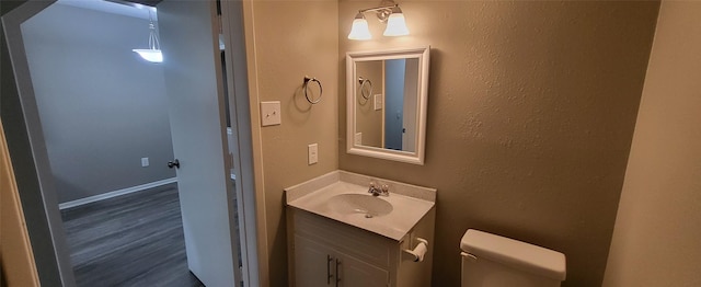 half bath featuring toilet, a textured wall, wood finished floors, and vanity