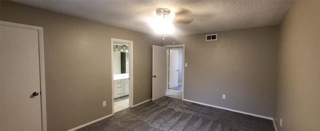 unfurnished bedroom featuring baseboards, visible vents, ensuite bath, a textured ceiling, and dark carpet