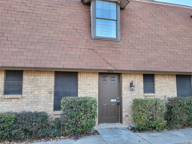 property entrance with brick siding and roof with shingles