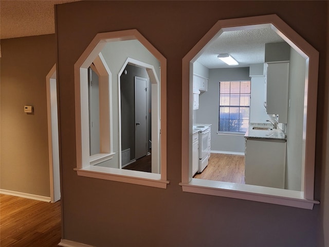 additional living space featuring a textured ceiling, light wood-type flooring, and baseboards