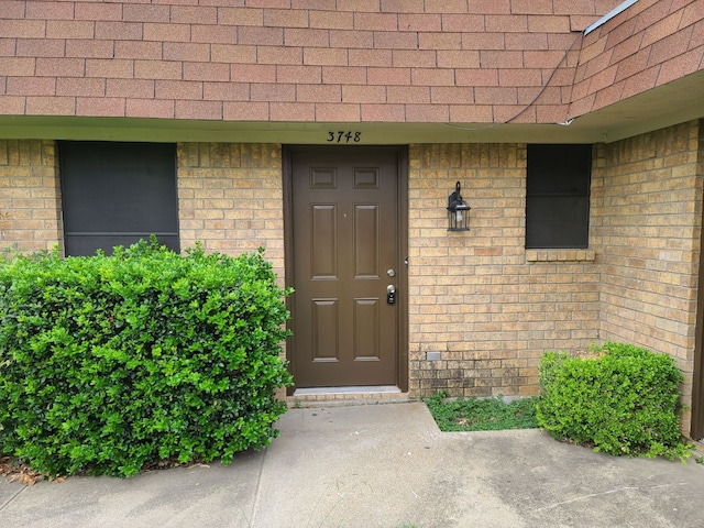 entrance to property with a shingled roof and brick siding