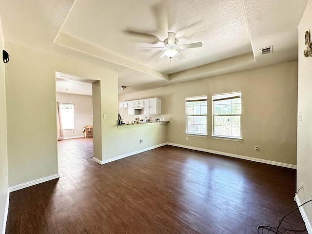 spare room with dark hardwood / wood-style flooring, a textured ceiling, a raised ceiling, and ceiling fan