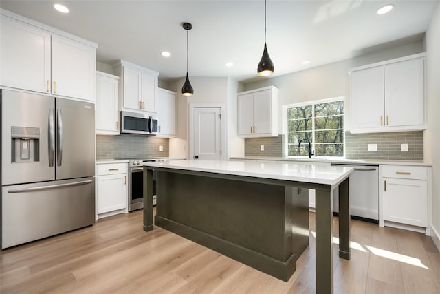 kitchen with stainless steel appliances, white cabinets, a kitchen island, decorative light fixtures, and light wood-type flooring