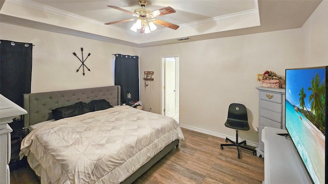 bedroom featuring a raised ceiling, ornamental molding, ceiling fan, and light wood-type flooring