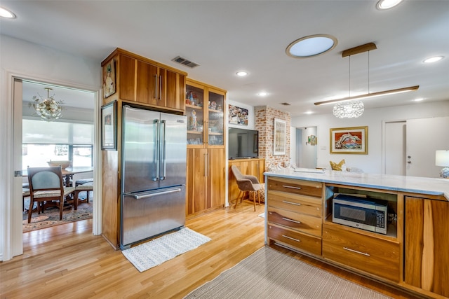 kitchen with decorative light fixtures, stainless steel appliances, and light hardwood / wood-style flooring