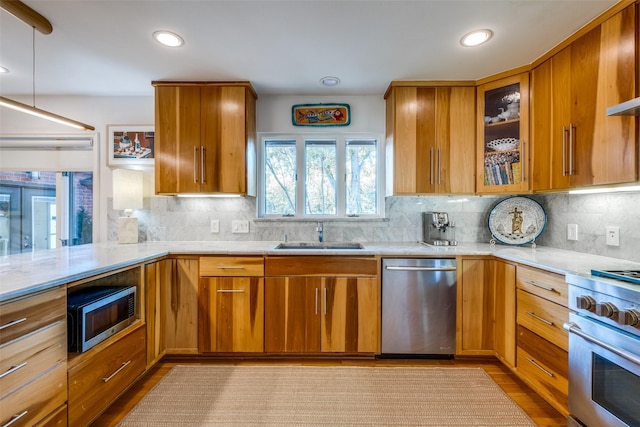 kitchen with hanging light fixtures, stainless steel appliances, light hardwood / wood-style flooring, sink, and backsplash