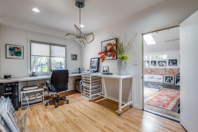 home office with light hardwood / wood-style flooring and a skylight