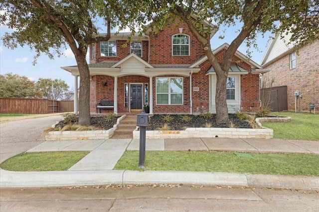 view of front of property featuring a porch, brick siding, and fence