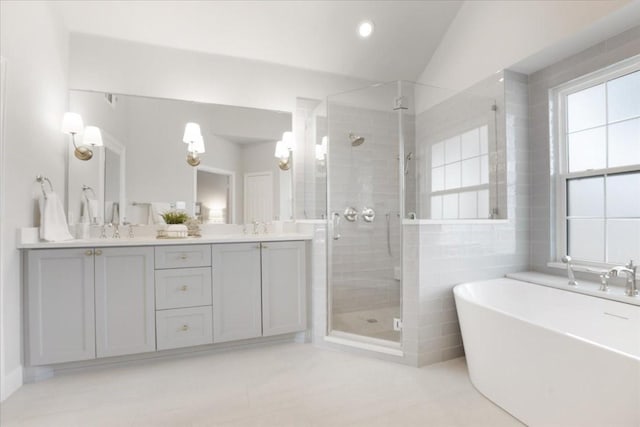 full bath with double vanity, a stall shower, a sink, a freestanding bath, and tile walls