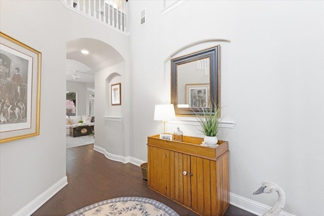 hallway featuring arched walkways, dark wood-style flooring, visible vents, a high ceiling, and baseboards