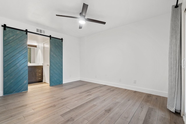 unfurnished bedroom with ceiling fan, a barn door, light wood-type flooring, and ensuite bathroom