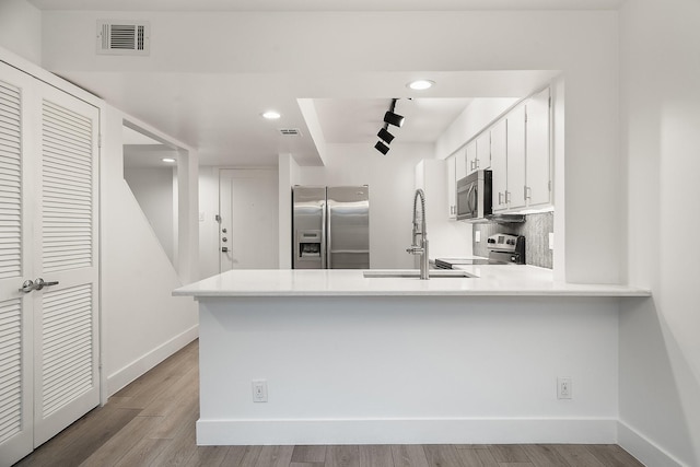 kitchen featuring appliances with stainless steel finishes, light wood-type flooring, sink, white cabinetry, and kitchen peninsula