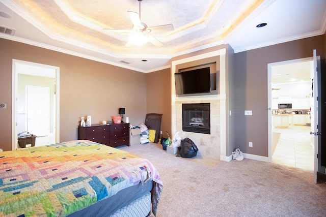 carpeted bedroom featuring a tray ceiling, ornamental molding, and a fireplace