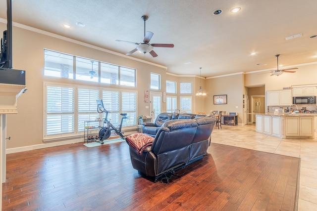 living room featuring ceiling fan, ornamental molding, light hardwood / wood-style floors, and a towering ceiling