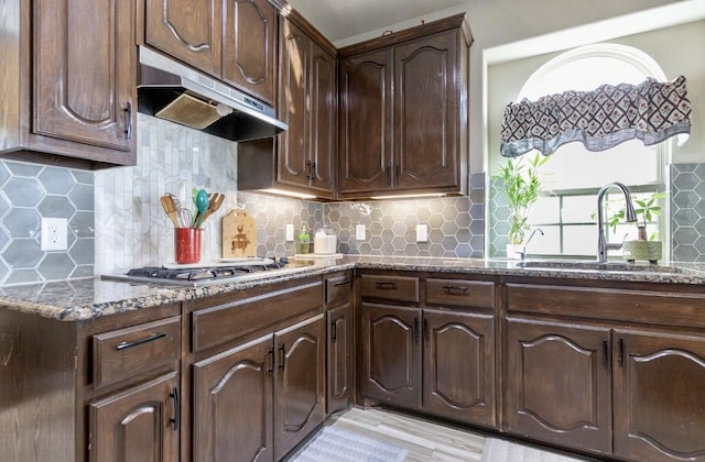 kitchen featuring dark stone countertops, stainless steel gas cooktop, sink, dark brown cabinetry, and decorative backsplash