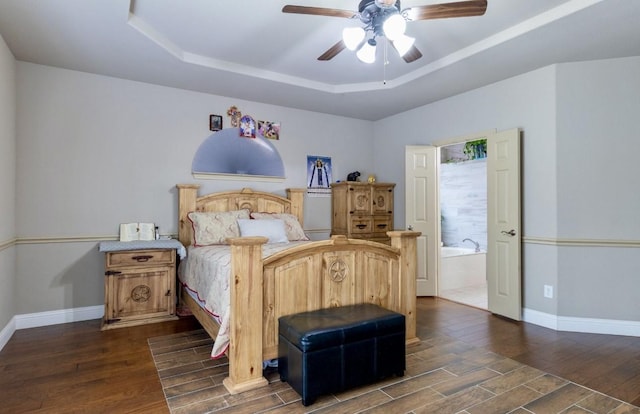 bedroom featuring a tray ceiling, ensuite bath, dark hardwood / wood-style floors, and ceiling fan