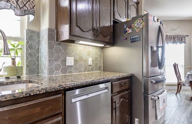 kitchen featuring appliances with stainless steel finishes, stone countertops, dark brown cabinetry, backsplash, and sink