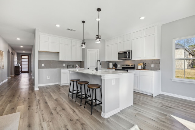 kitchen with appliances with stainless steel finishes, an island with sink, and white cabinetry