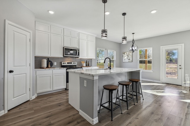 kitchen with a kitchen island with sink, hanging light fixtures, sink, appliances with stainless steel finishes, and white cabinets