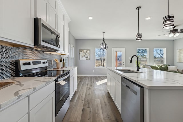 kitchen featuring an island with sink, white cabinetry, hanging light fixtures, sink, and appliances with stainless steel finishes