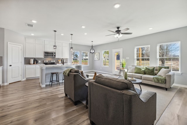 living room featuring sink, ceiling fan, and light wood-type flooring