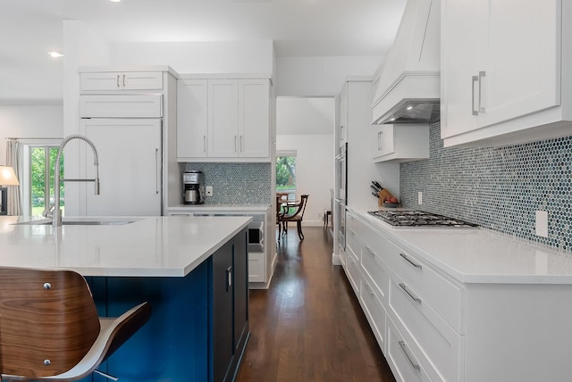 kitchen featuring a breakfast bar area, premium range hood, white cabinetry, light countertops, and appliances with stainless steel finishes