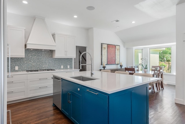 kitchen featuring an island with sink, custom range hood, light countertops, blue cabinetry, and a sink