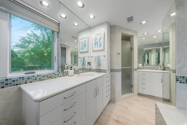 full bath with a shower stall, visible vents, two vanities, and a sink