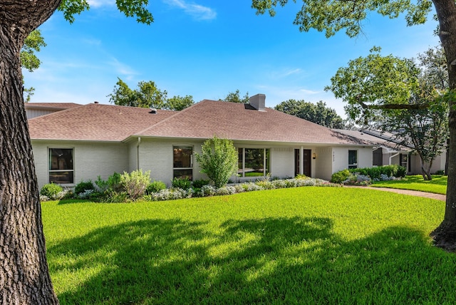 ranch-style home with a front yard, brick siding, a chimney, and roof with shingles