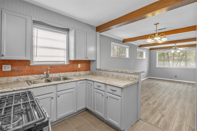 kitchen with sink, range with gas stovetop, kitchen peninsula, hanging light fixtures, and beam ceiling