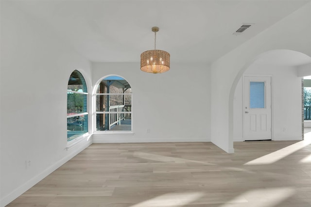 empty room featuring arched walkways, light wood finished floors, visible vents, an inviting chandelier, and baseboards