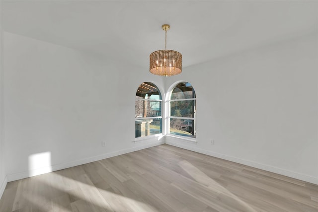 unfurnished room with a chandelier, baseboards, and light wood finished floors