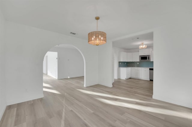 unfurnished living room with light wood finished floors, visible vents, arched walkways, baseboards, and an inviting chandelier