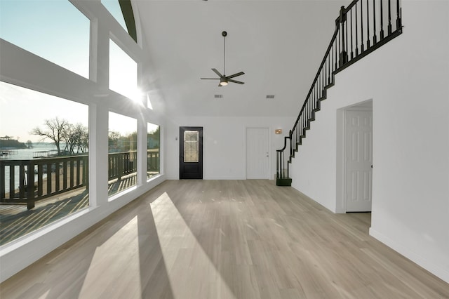 unfurnished living room featuring baseboards, a towering ceiling, ceiling fan, stairs, and light wood-type flooring