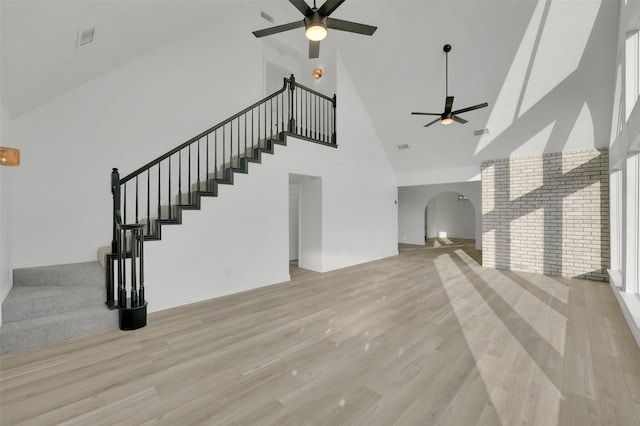 unfurnished living room with arched walkways, light wood finished floors, visible vents, stairway, and ceiling fan