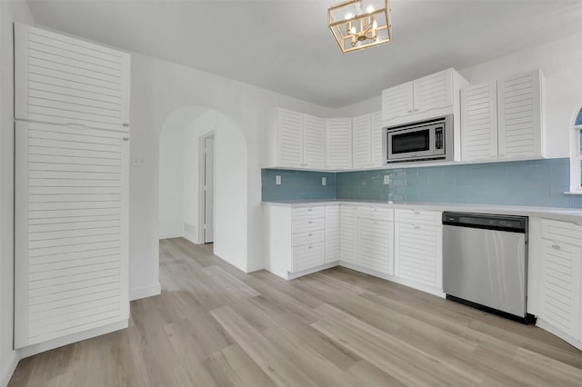 kitchen featuring arched walkways, decorative light fixtures, light countertops, appliances with stainless steel finishes, and white cabinets