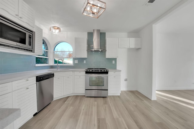 kitchen featuring wall chimney range hood, appliances with stainless steel finishes, light countertops, and a sink