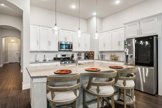 kitchen featuring stainless steel appliances, an island with sink, white cabinets, and hanging light fixtures