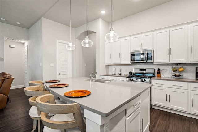 kitchen featuring a breakfast bar area, dark wood-type flooring, a sink, stainless steel appliances, and backsplash
