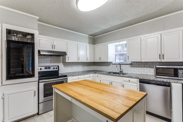 kitchen with appliances with stainless steel finishes, white cabinets, wood counters, a kitchen island, and sink