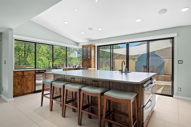 kitchen featuring a center island with sink, lofted ceiling, oven, fridge, and a kitchen bar