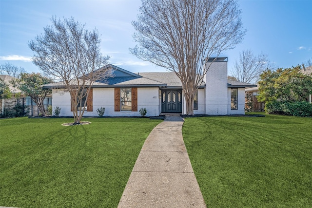 single story home featuring brick siding, a chimney, a shingled roof, a front yard, and fence